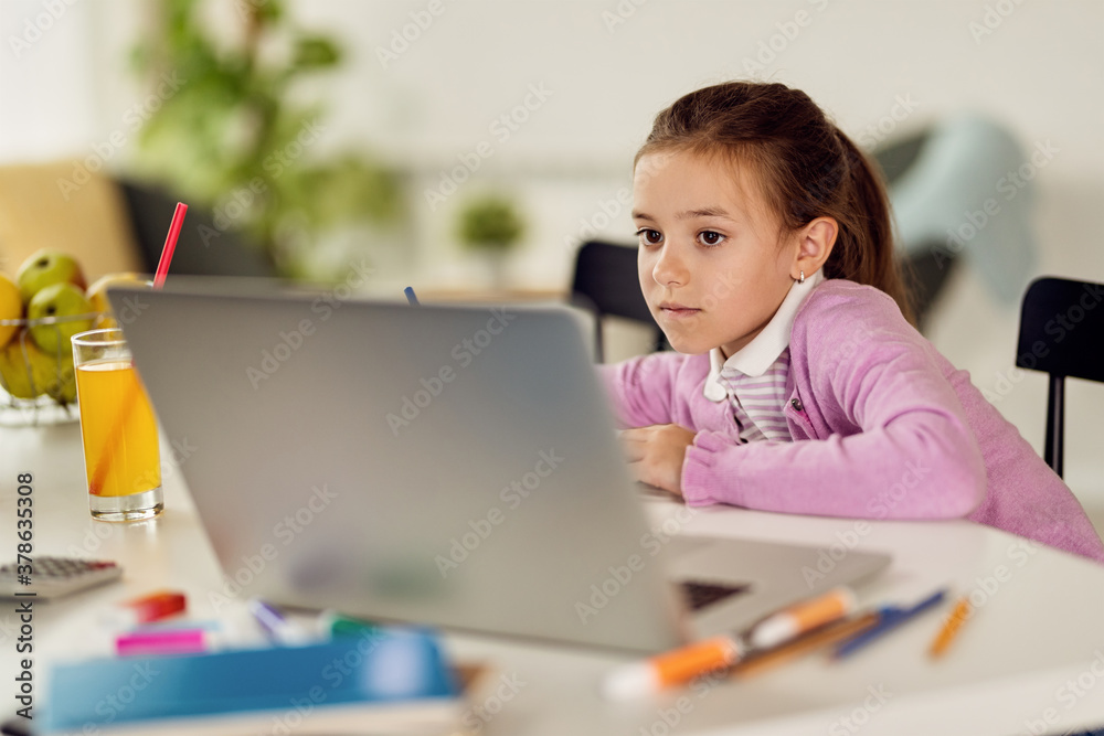 Little girl using computer while doing her homework. Little girl using computer while doing her homework.