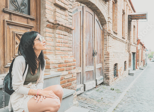 Brunette female tourist sits on the stairs and admires historical buildings of Telavi city in Georgia. photo