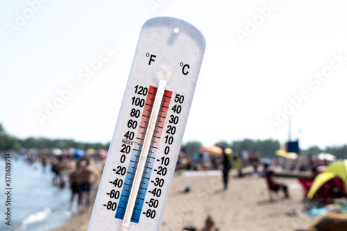 A thermometer held up over a a hot crowded beach, reading about 90 degrees Fahrenheit 30 degrees Celsius