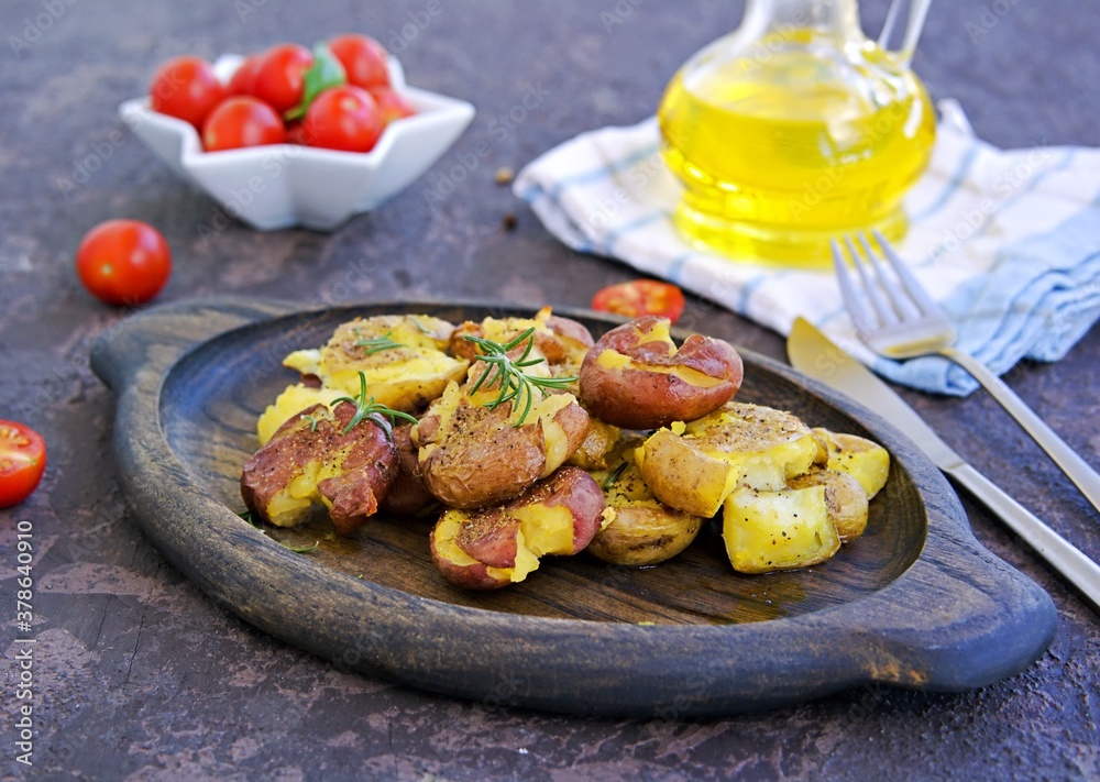 Crash Hot Potatoes, boiled potatoes in a peel, crushed and baked with olive oil and herbs on a wooden plate on a dark concrete background. Australian cuisine. Potato recipes. Crash Hot Potatoes, boiled potatoes in a peel, crushed and baked with olive oil and herbs on a wooden plate on a dark concrete background. Australian cuisine. Potato recipes.