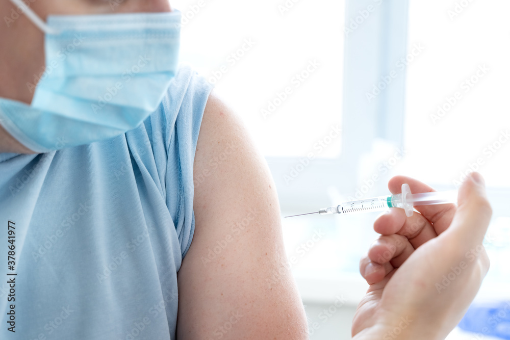 Man, adult in face mask in doctor's office is vaccinated. Syringe with vaccine for covid-19 coronavirus,flu,dangerous infectious diseases. Injection after clinical trials for human, child. Medicine Man, adult in face mask in doctor's office is vaccinated. Syringe with vaccine for covid-19 coronavirus,flu,dangerous infectious diseases. Injection after clinical trials for human, child. Medicine