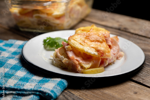 Scalloped potatoes with ham and cheese on wooden background