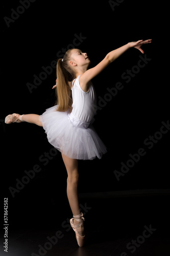 Cute little girl in a tutu and pointe shoes is dancing in the studio on a black background.