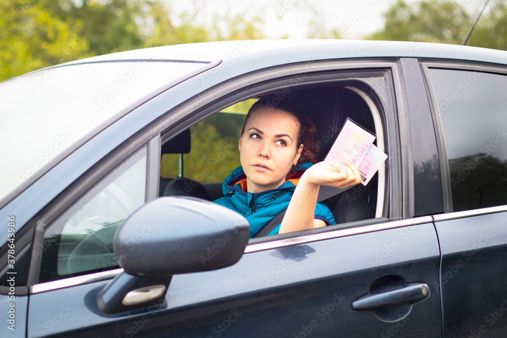 Serious woman holding out driver's license and car documents, driving her car. Traffic violation concept, stop, document check