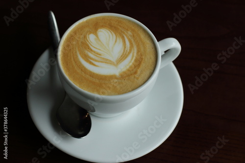 Coffee with foam in white cup in black light, dark background, flower foam on top 