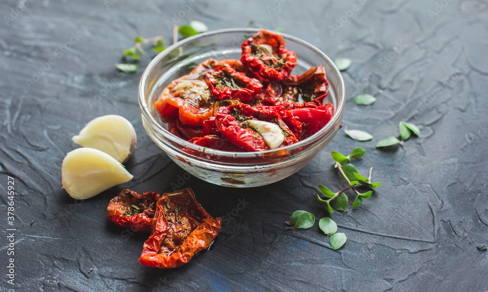 Dried tomatoes with garlic and olive oil in a bowl on a gray table background Dried tomatoes with garlic and olive oil in a bowl on a gray table background
