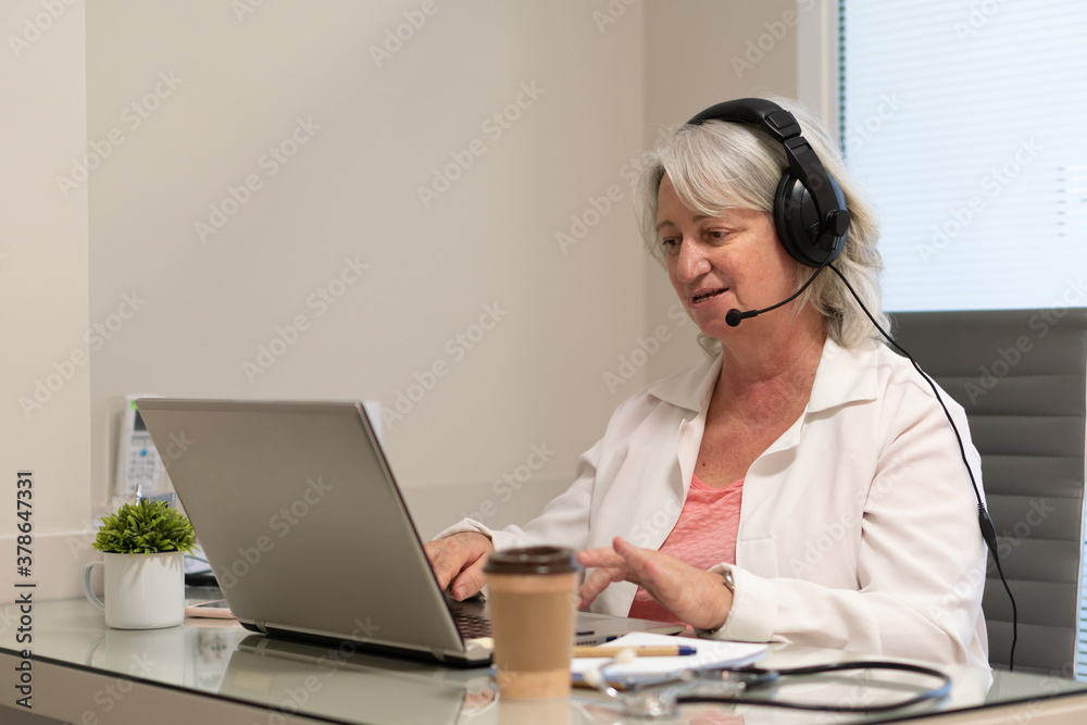 Confident mature female doctor with headset taking an online medical appointment at medical clinic healthcare, clinic, treatment concept.. Confident mature female doctor with headset taking an online medical appointment at medical clinic healthcare, clinic, treatment concept..