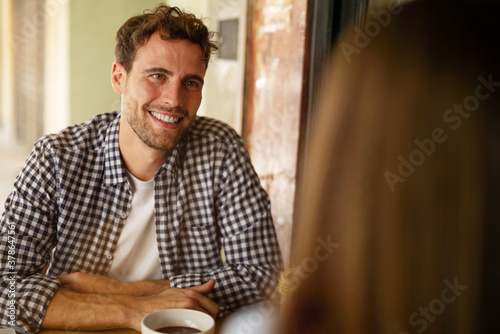 An young carefree romantic happy couple in love is having fun and drinking coffee while enjoying a breakfast together in city center cafeteria on a weekend in a sunny day.