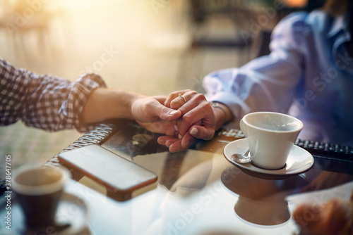 An authentic close up shot of a young man is caressing a hand of his a beloved woman while enjoying a romantic breakfast together in the city center cafeteria on a weekend in a sunny day.
