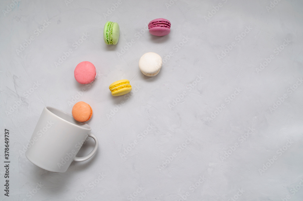 Colorful appetizing delicious crunchy macaroons spilling out of the gray mug on the table. Colorful appetizing delicious crunchy macaroons spilling out of the gray mug on the table.