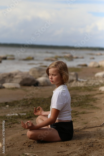 The girl sits on the sandy shore in the lotus position. photo