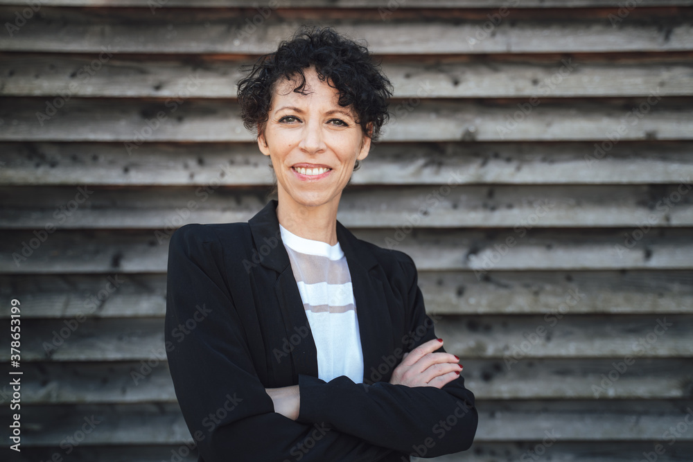 Portrait of smiling female entrepreneur standing arms crossed against shutter wall Portrait of smiling female entrepreneur standing arms crossed against shutter wall