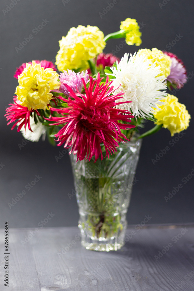 fresh colorful asters bouquet in cristal vase on black background