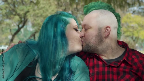 Dolly in shot of a couple of alternative people sitting on a bench and kissing 