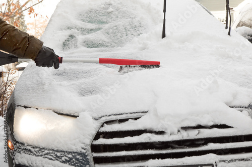 Fotografija winter driving safety - a driver brushing piled up snow from the hood of the car
