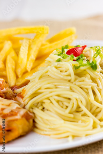 Spaghetti with slices of chive and spice. Chicken with cheese and french fries. Selective focus