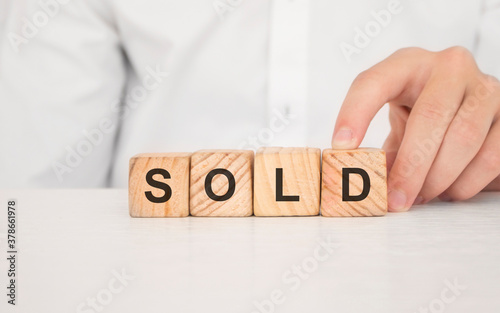 Close up young man's hand in white shirt wooden block cube for Sold wording on white marble table floor