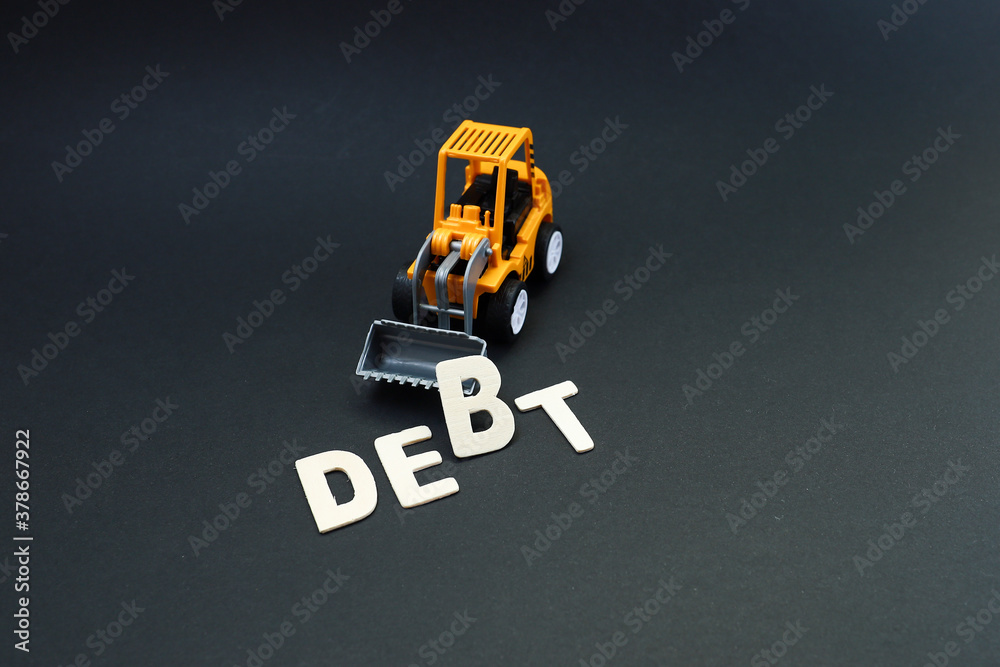 Obraz premium Block letters on debt lifted by a toy bulldozer on black background