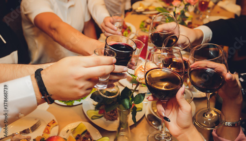 Close up shot of group of people clinking glasses with wine or champagne in front of bokeh background. older people hands. photo