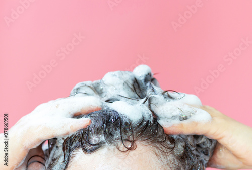 A girl washes her hair with shampoo on pink background, front view