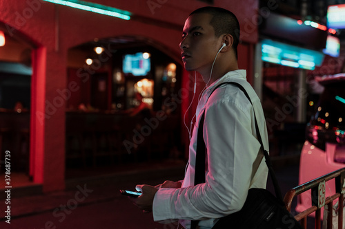 Fotografija Business man listen to music with earphones at night street market
