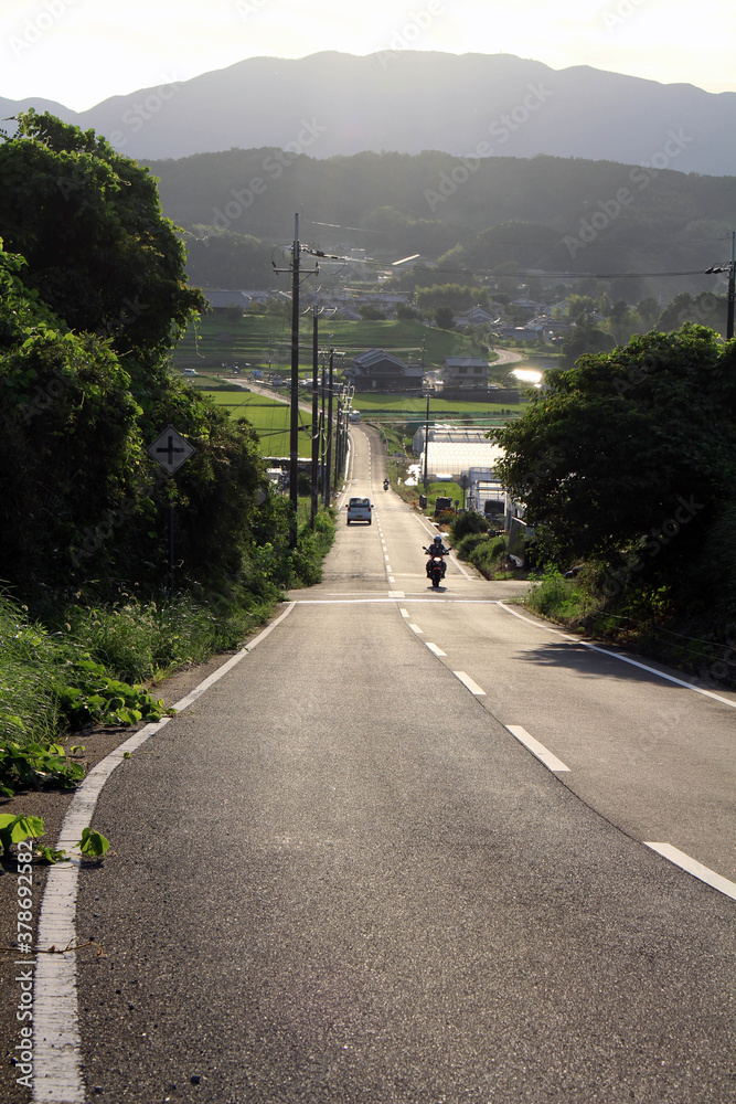 Fototapeta premium People driving motorcycle in countryside with mountains as background in Asuka
