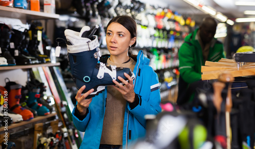 Glad girl choosing ski boots for skiing in store of sports equipment