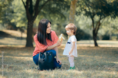 Mother Feeding Toddler a Banana Snack Outdoors in the Park photo