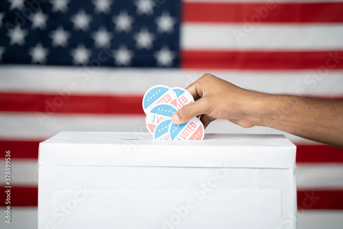Konstfotografi Close up of Hands dropping multiple I Voted sticker inside Ballot box with US flag as background, Concept of fraud in USA elections