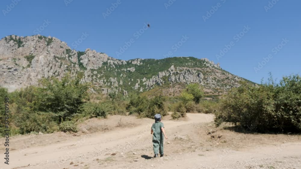 boy child in a green jumpsuit carries a stone while in the mountains in the summer boy child in a green jumpsuit carries a stone while in the mountains in the summer