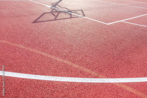 White lines on outdoor basketball field and shadow of the rack with a shield and basketball ring during sunny day outdoors