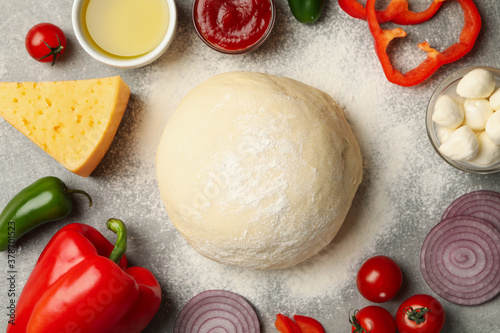 Dough and ingredients for cooking pizza on gray background