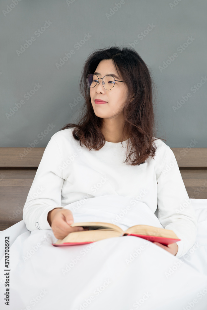 Pretty female sitting on bed holding a book in hand Pretty female sitting on bed holding a book in hand