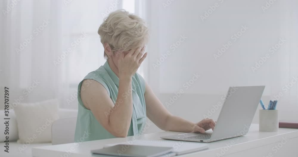 middle-aged woman with headache is working with laptop in home, touching forehead by hands, tired middle-aged woman with headache is working with laptop in home, touching forehead by hands, tired