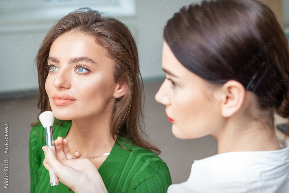 Make up artist applying professional make up of tonal foundation on the face of beautiful young caucasian woman in make up room. Base for make up. Make up artist applying professional make up of tonal foundation on the face of beautiful young caucasian woman in make up room. Base for make up.