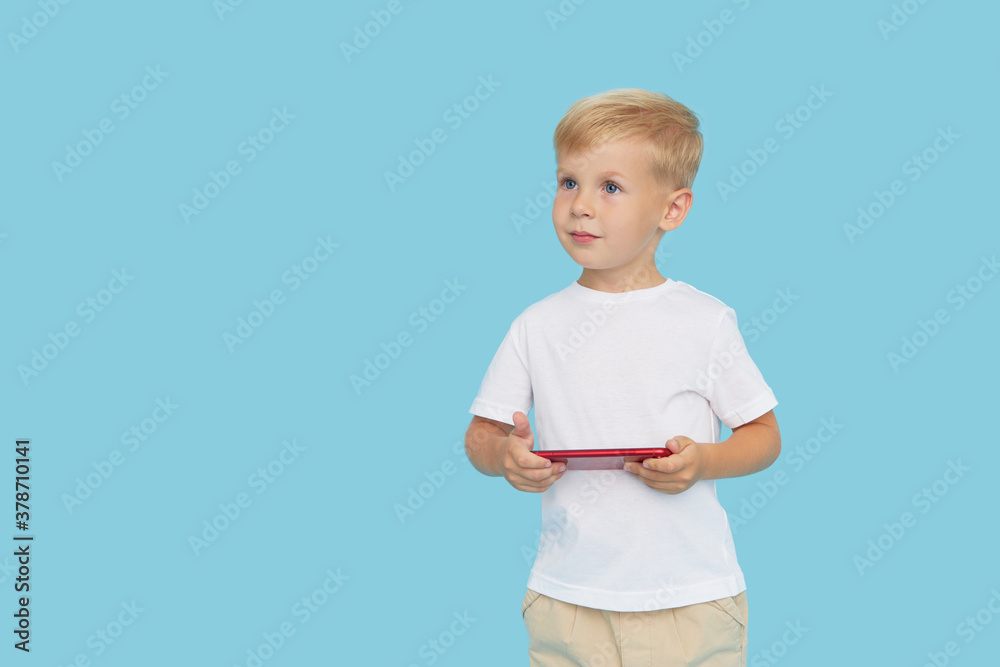 Cute smilling child boy with smartphone on blue background. Advertising of educational applications on a mobile phone for children. Funny face. Cute smilling child boy with smartphone on blue background. Advertising of educational applications on a mobile phone for children. Funny face.