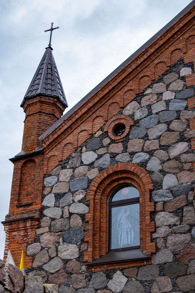 Cross on the tower. Brick wall. Gothic Church of the Virgin Mary made of stone and brick in the city of Braslav, Belarus