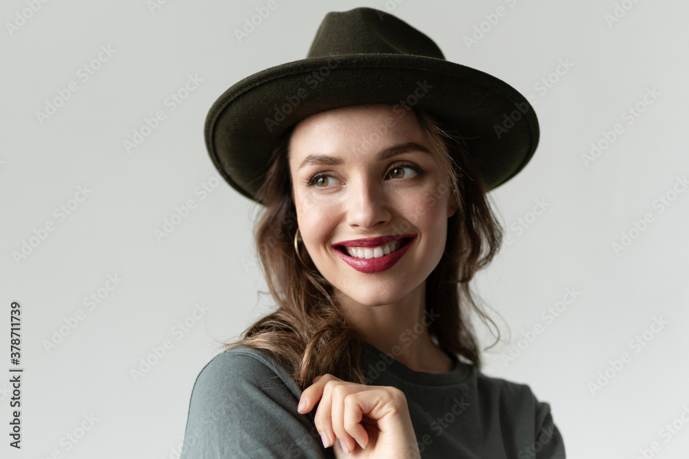 Portrait of woman with perfect smile wearing stylish black hat, posing in studio isolated on gray background. Trendy accessories. Photography for advertising or beauty blogging Portrait of woman with perfect smile wearing stylish black hat, posing in studio isolated on gray background. Trendy accessories. Photography for advertising or beauty blogging