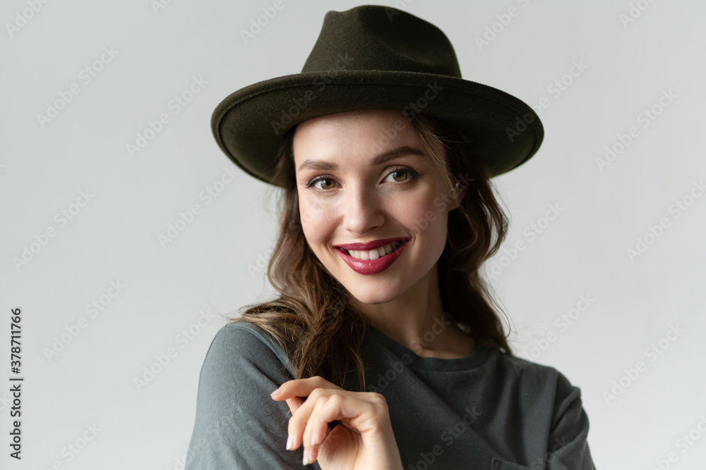 Close up portrait of young smiling millenial woman wearing stylish black hat and looking at camera in studio isolated on gray background. Trendy autumn accessories. Perfect smile and body language Close up portrait of young smiling millenial woman wearing stylish black hat and looking at camera in studio isolated on gray background. Trendy autumn accessories. Perfect smile and body language