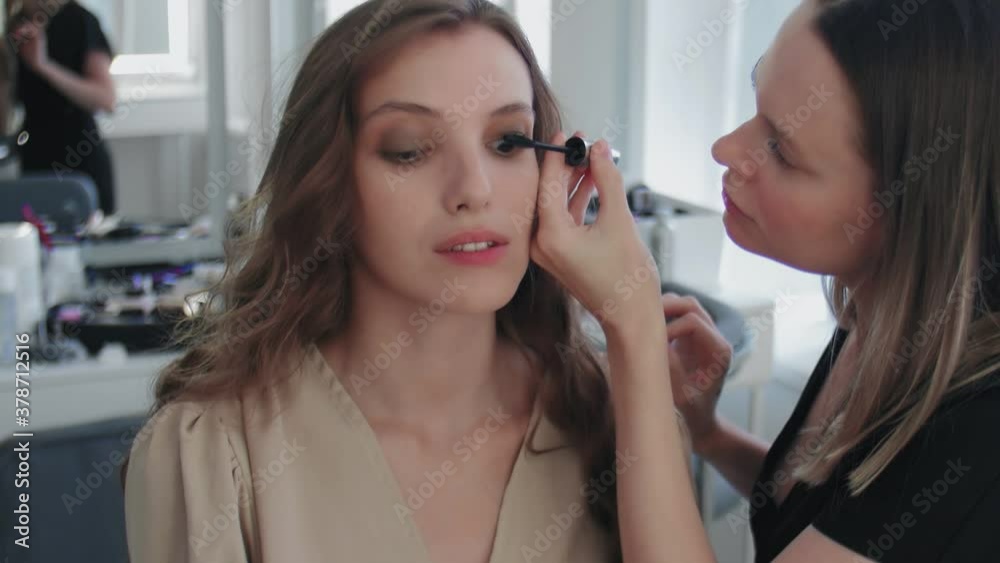 Process of Professional Makeup for beautiful and young woman sitting at the Studio. Make up Artist applies mascara to model Process of Professional Makeup for beautiful and young woman sitting at the Studio. Make up Artist applies mascara to model