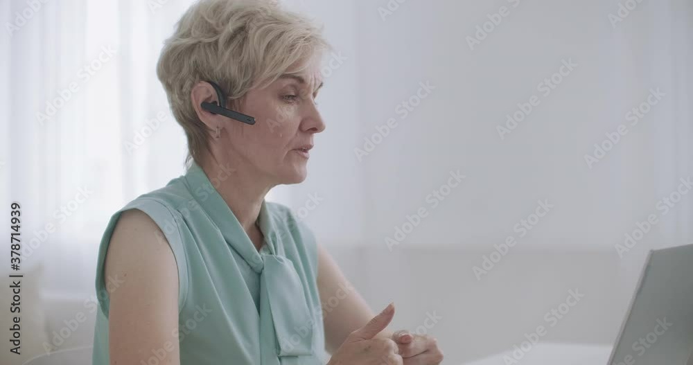 aged lady is communicating online by videocall, using headset and notebook, online consultation and distant work aged lady is communicating online by videocall, using headset and notebook, online consultation and distant work