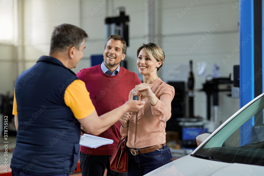 Obraz premium Happy couple giving car key to their mechanic in auto repair shop.