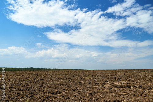 plowed field and blue sky, soil and clouds of a bright sunny day - concept of agriculture