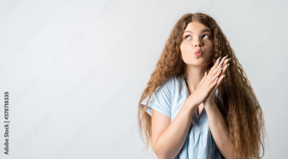 Young woman looks with dreamy expression aside, stands against white wall with free space for text Young woman looks with dreamy expression aside, stands against white wall with free space for text