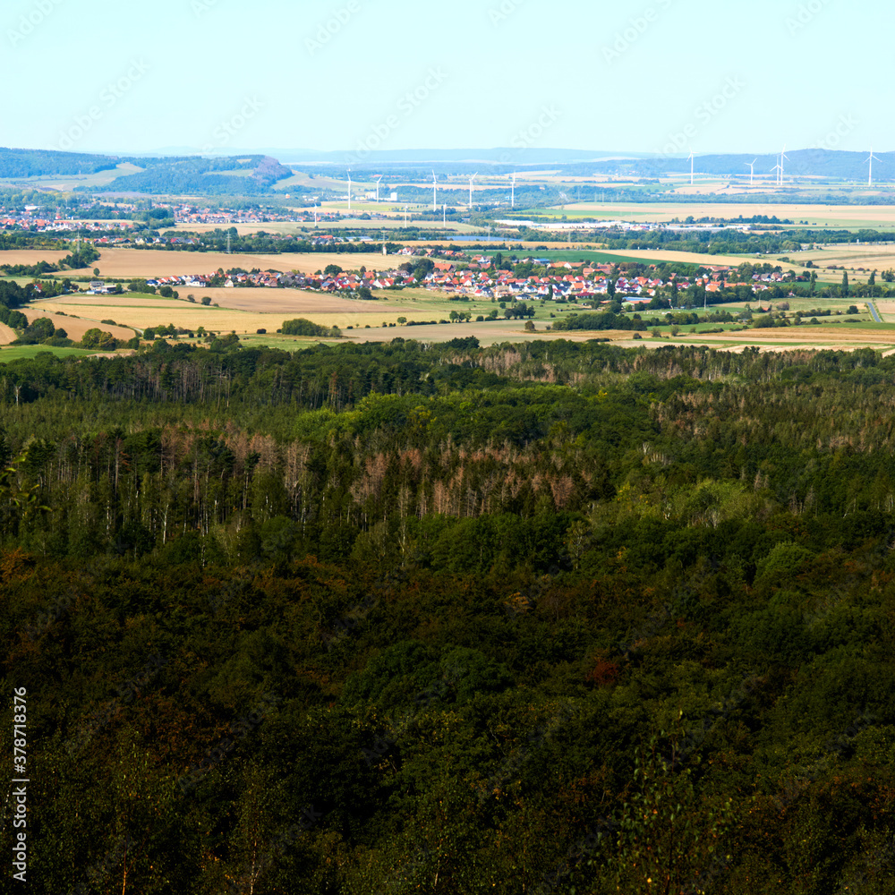 View over the dense green forest in the Harz Mountains to a village near Bad Harzburg with wind turbines in the background