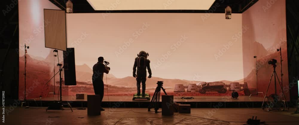 Behind the scenes shot of virtual production stage with huge LED screens, cinematorgapher shooting Mars scene. Future of movie production