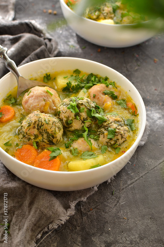Meatball soup with noodles and carrots. Dark gray background. Gray linen napkin. Close-up. Healthy lunch, soup with herbs and meat. Vertical view