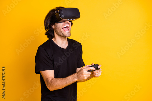 Profile photo of young man virtual reality hold controller open mouth wear vr helmet t-shirt isolated yellow color background