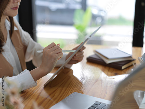 Side view of female hands using digital tablet with stylus on wooden table