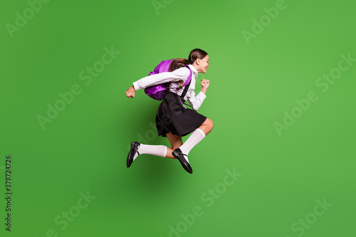 Photo portrait of brunette girl with pigtails running to school jumping up with pink backpack isolated on vivid green colored background photo